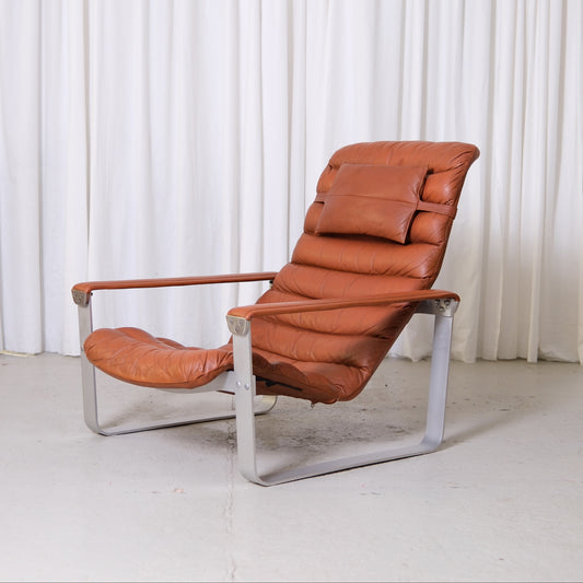 Vintage Ilmari Lappalainen Pulkka lounge chair in brown leather with grey metal frame photographed in studio setting.