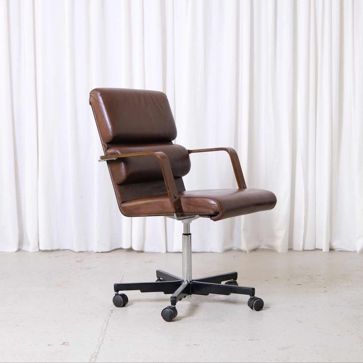 Yrjö Kukkapuro Plaano office chair in brown leather with wooden armrests and swivel base with castors.