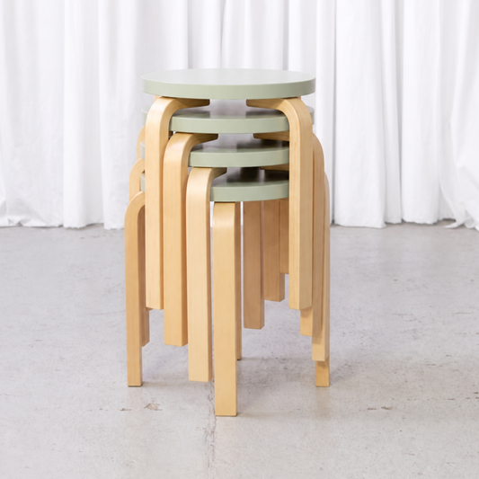 Four Artek E60 stools with mint-green seats stacked in a studio