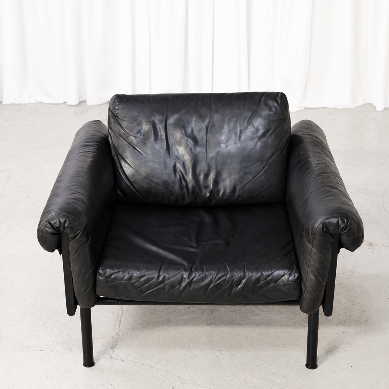 Black leather seat, back cushion and padded arms of a vintage Ateljee armchair